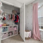 A neatly organized children's closet with clothes, toys, and pink decor in a bright room.