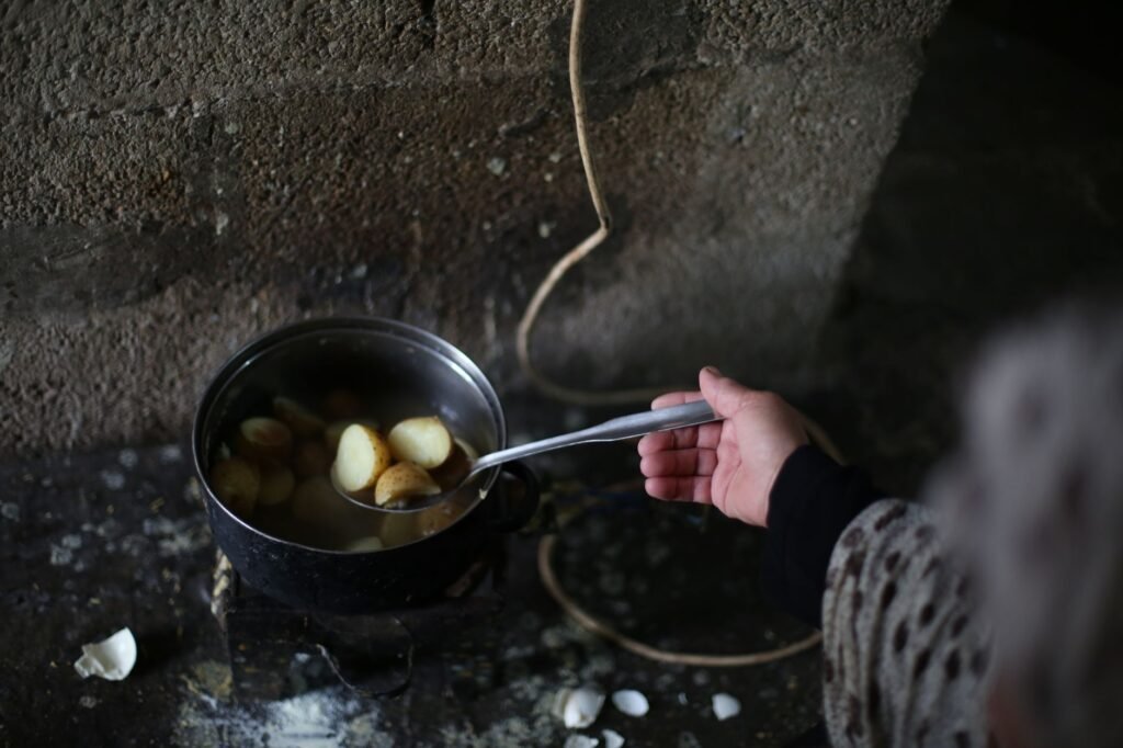 A hand stirring boiled potatoes in a pot against a rustic backdrop, highlighting traditional cooking.