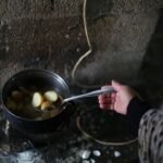 A hand stirring boiled potatoes in a pot against a rustic backdrop, highlighting traditional cooking.
