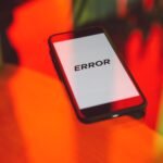 A smartphone displaying an 'ERROR' message surrounded by vibrant red and green reflections indoors.