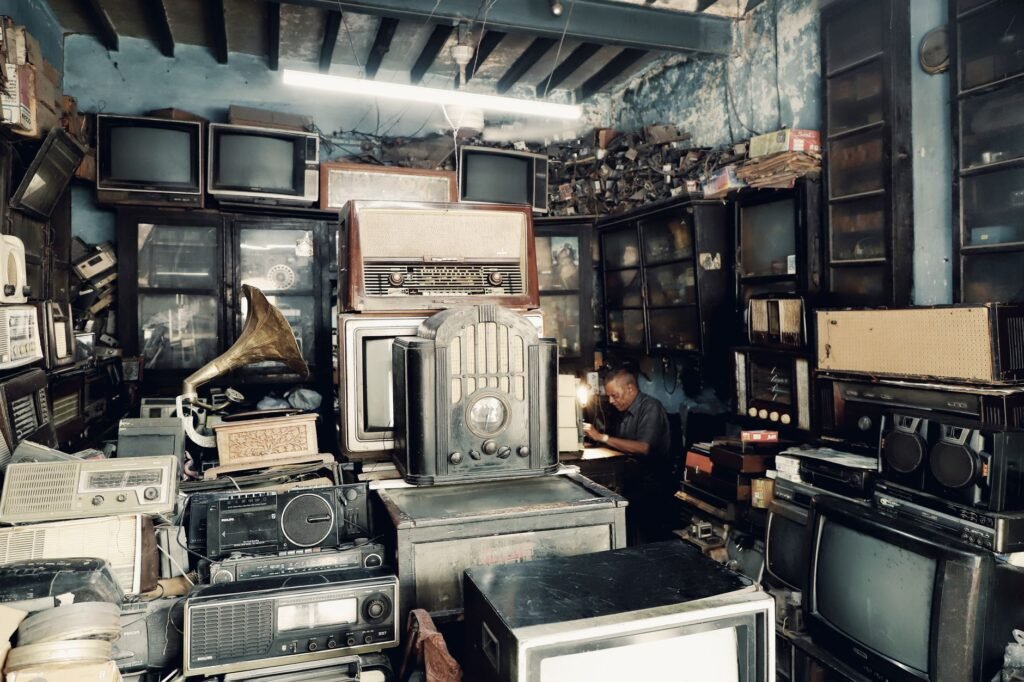 A cluttered vintage shop filled with antique radios, TVs, and a man working in the background.