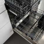 A clean and empty stainless steel dishwasher open in a modern kitchen setting.