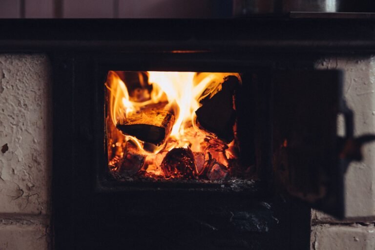 A close-up of a wood-burning fireplace emitting warmth with flickering flames and glowing embers.