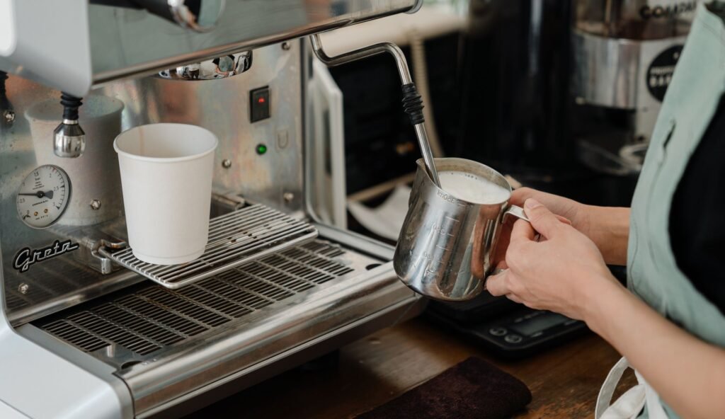 Side view of crop anonymous worker whipping milk using coffeemaker while preparing coffee in modern cafe