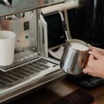Side view of crop anonymous worker whipping milk using coffeemaker while preparing coffee in modern cafe