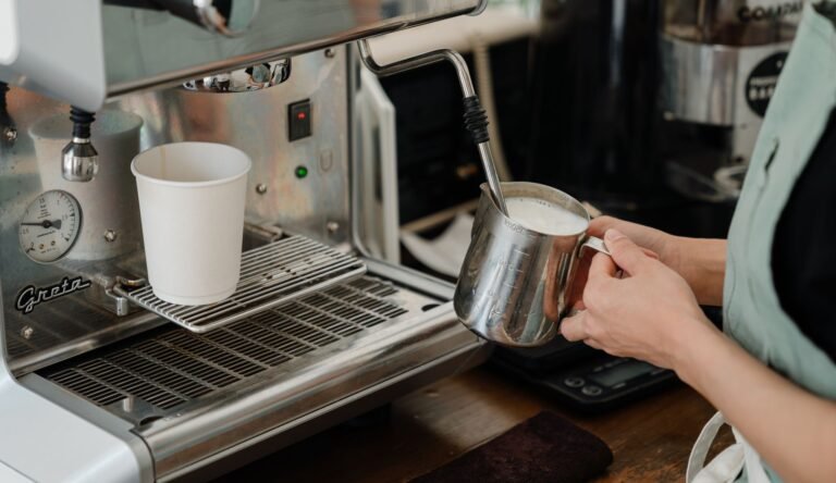 Side view of crop anonymous worker whipping milk using coffeemaker while preparing coffee in modern cafe