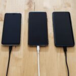 Three smartphones connected to chargers on a wooden surface, showcasing modern technology