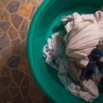 Top view of a laundry basket filled with crumpled clothes on a tiled floor.