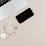 Flat lay of a laptop, smartphone, and charger on a beige background showcasing modern technology essentials.