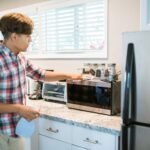 A man is cleaning a microwave in his modern kitchen using a spray bottle and cloth.
