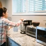 Woman cleaning a coffee maker in a bright, modern kitchen with appliances.