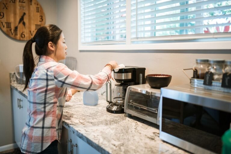 Woman cleaning a coffee maker in a bright, modern kitchen with appliances.