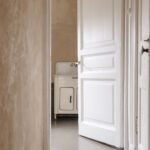 A rustic interior with a white wooden door slightly ajar revealing a vintage sink inside.