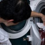 Close-up of a man placing clothes into a washing machine during household chores.