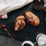 Delicious grilled chicken breasts served with spices, oil, and sauces on a slate plate.