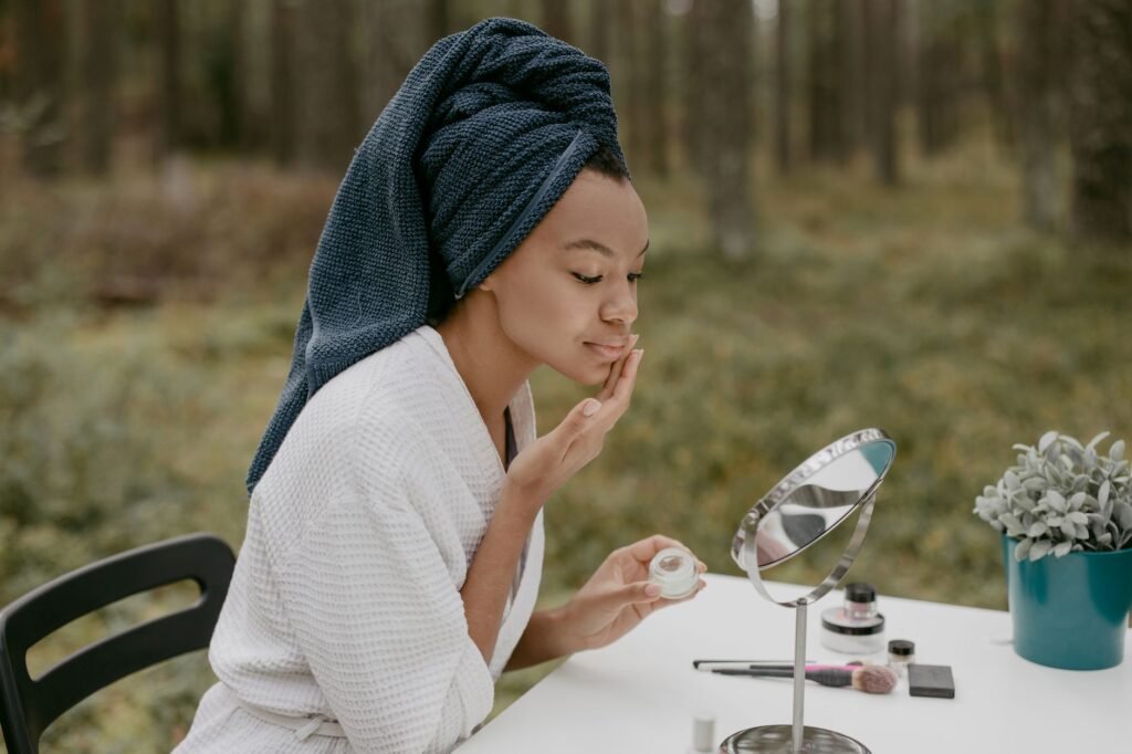 A woman in a bathrobe applies face cream in a serene outdoor environment.