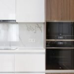 Modern interior of white and wooden kitchen with cabinets cupboards and built in appliances in contemporary flat