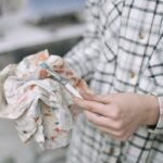 Close-up image of an artist in plaid shirt cleaning a paintbrush with a colorful cloth