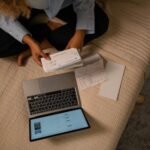 Overhead view of woman organizing finances on bed with laptop and checks.