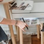 High angle of crop anonymous female photographer using printer for making images while working in flat