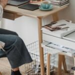 High angle of crop anonymous female photographer working in netbook and printing photos while working at home