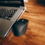 A wireless mouse and laptop placed on a polished wooden desk, perfect for office and remote work setup.