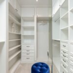 Soft blue velour pouf in white built in closet with empty shelves and racks in classic styled apartment