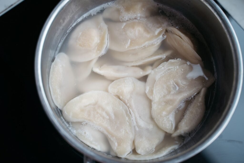Top view of dumplings boiling in a stainless steel pot with water.
