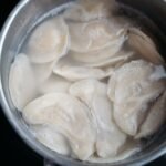Top view of dumplings boiling in a stainless steel pot with water.
