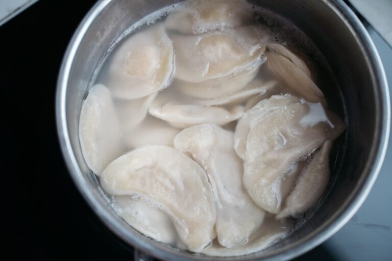 Top view of dumplings boiling in a stainless steel pot with water.