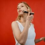 Woman uses a makeup brush to apply cosmetics in front of a vivid red background.