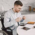 Man in wheelchair repairing electronics at home using tools, showcasing independence.