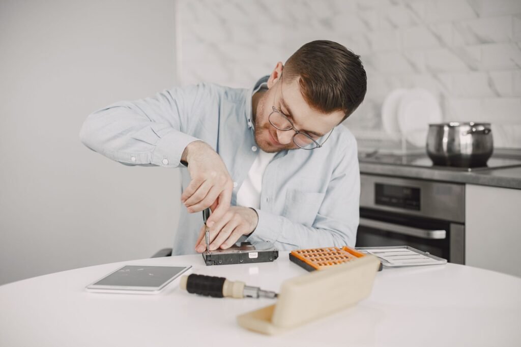 Man wearing glasses using a screwdriver to fix a device on a kitchen table.