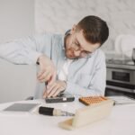 Man wearing glasses using a screwdriver to fix a device on a kitchen table.