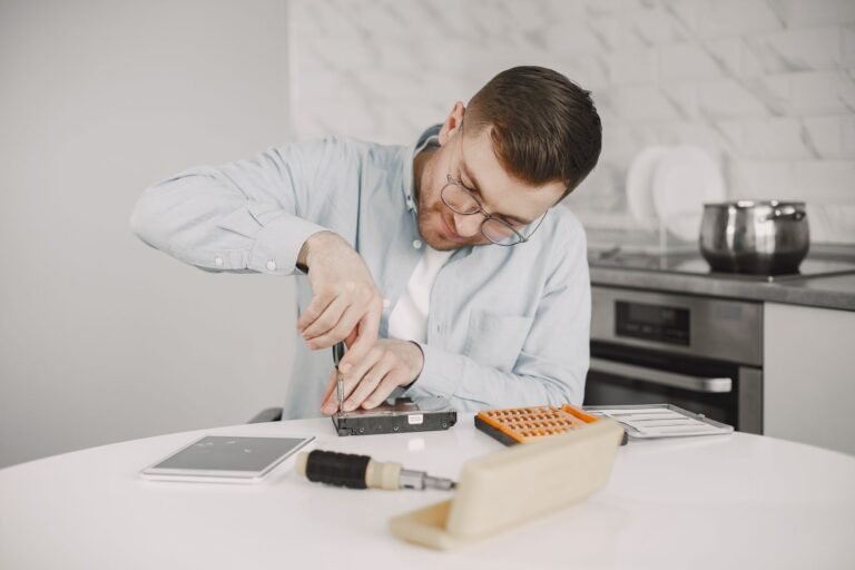 Man wearing glasses using a screwdriver to fix a device on a kitchen table.