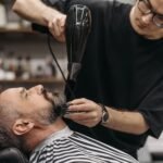 Barber styling a man's beard with hair dryer in a modern salon, capturing the art of grooming.