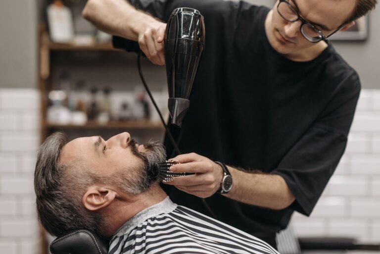 Barber styling a man's beard with hair dryer in a modern salon, capturing the art of grooming.