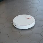 A sleek, white robotic vacuum cleaner operating on a hexagonal tiled floor.