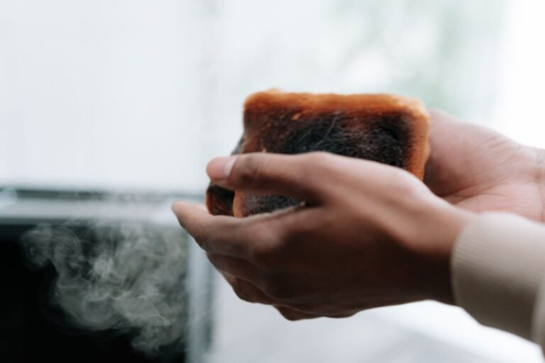 A close-up view of hands holding a toasted slice of bread with visible smoke and burnt texture.