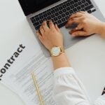 A woman using a laptop alongside a contract document on a desk, emphasizing business and legal themes.