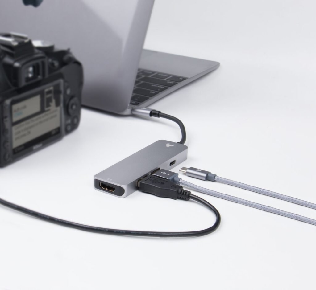 Close-up of a laptop, camera, and connected cables on a desk, depicting modern technology.