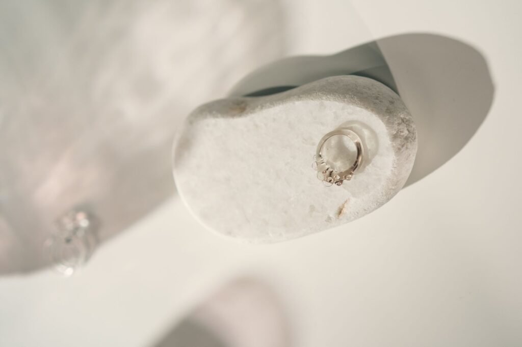 Minimalist silver ring displayed on a smooth white stone with soft lighting, perfect for jewelry showcases.