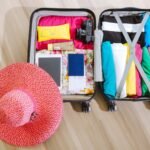 Top view of a suitcase packed with clothes, a camera, and a sun hat, ready for summer travel.