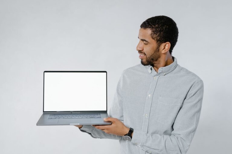 Man in striped shirt showcasing a laptop with blank screen against white background.