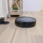 A sleek robotic vacuum navigates a clean hardwood floor beside a docking station.