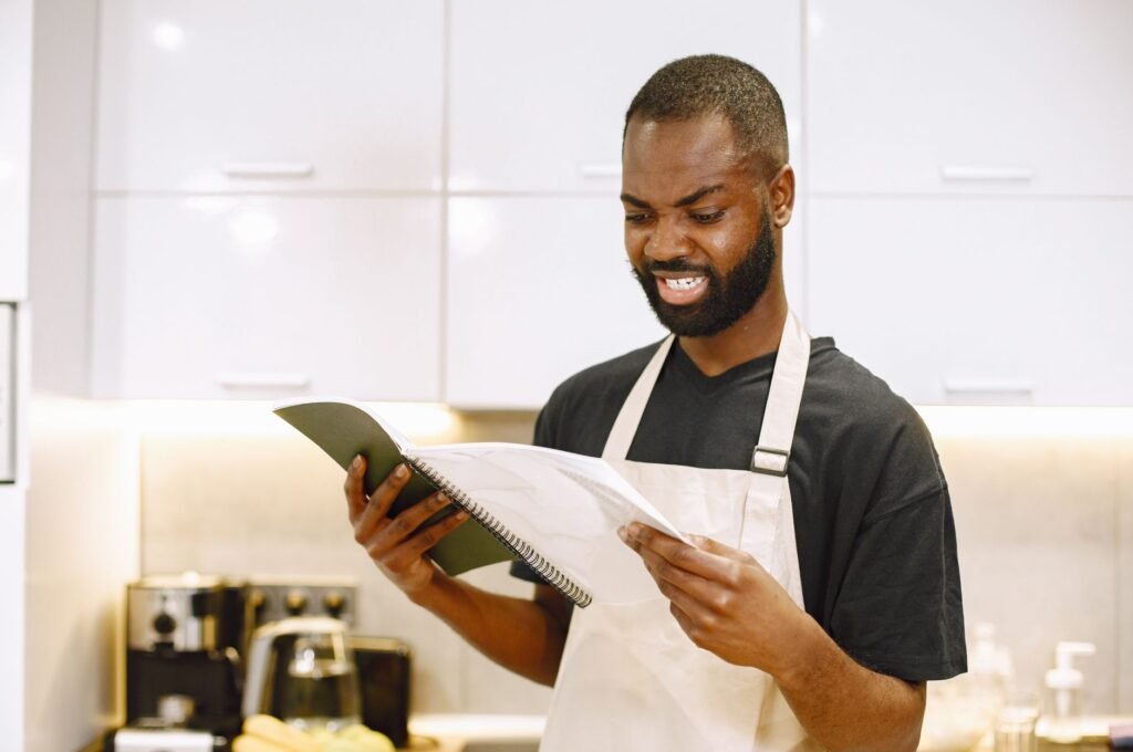 A chef wearing an apron looks puzzled while reading a recipe in a contemporary kitchen.