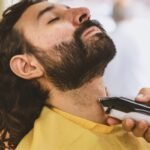 Close-up of a man getting his beard trimmed with an electric shaver.