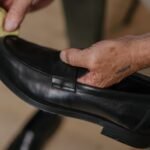 Detailed shot of hands polishing a black leather shoe with a cloth indoors.