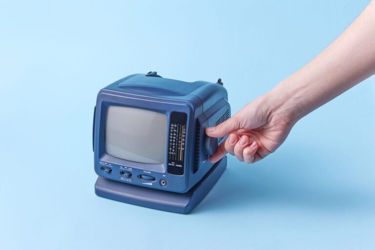 A hand is adjusting a vintage portable TV set against a blue background, highlighting retro technology.
