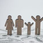 Wooden family figurines on dollar bills symbolizing financial stability.